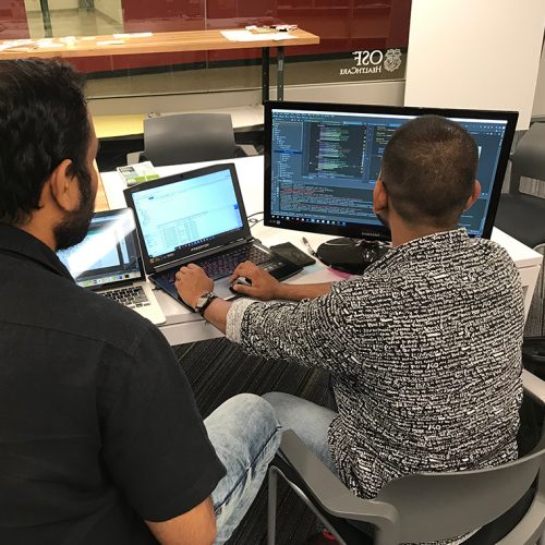two males working on laptop with second monitor